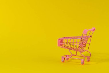 Sarı arka planda boş pembe minyatür alışveriş arabası. Sezonluk satış, kopyalama alanı