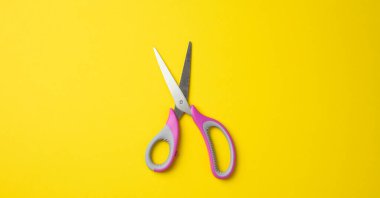 Sarı zemin üzerinde pembe plastik saplı metal makas, üst görünüm
