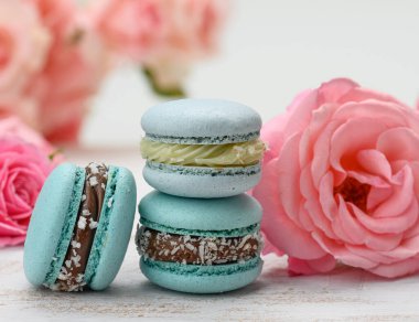 Beyaz masa ve pembe gül tomurcukları üzerinde bir yığın mavi badem kurabiyesi, lezzetli bir tatlı.