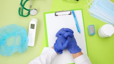 top view of the doctor's desk, who is bent over in a prayer position, wearing blue latex gloves, workplace
