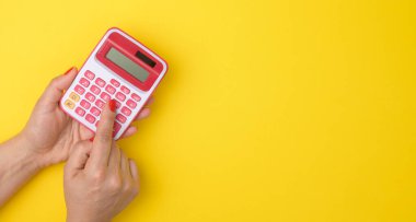 female hand holding a pink calculator on a yellow background, copy space, banner