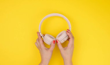 İki kadın el, sarı arka planda pembe kablosuz kulaklık tutuyor.