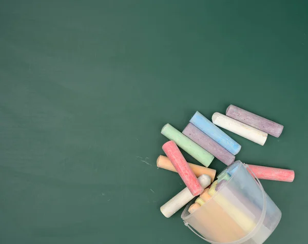 multicolored crayons on the background of green chalk school blackboard, copy space