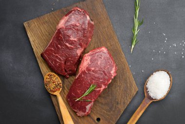 Klasik bifteğin çiğ parçaları ahşap bir tahtanın üzerinde duruyor, siyah masa, üst manzara.