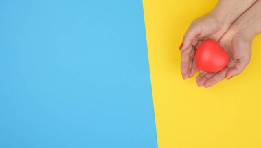 Kadın elleri kırmızı kalbi, mavi arkaplanı tutar. Aşk ve bağış konsepti, kopyalama alanı