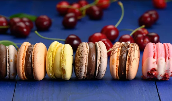 Multicolored Macarons Ripe Red Cherries Blue Wooden Background Close — Stock Photo, Image