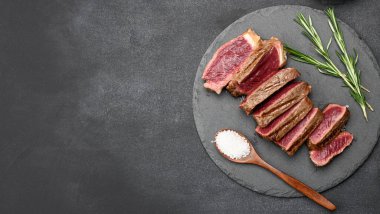 Kızarmış biftekler siyah bir tahtada parçalara bölünmüş, kan, üst manzara, kopyalama alanı...