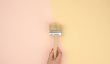 Kadın eli yeni boya fırçasının ahşap sapı pembe arka planda, kopyalama alanı