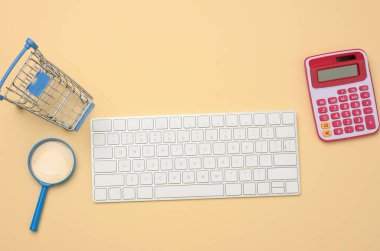 Beyaz kablosuz klavye ve boş alışveriş arabası, bej arka planda büyüteç, bütçe analiz konsepti, tasarruf. İnternetten alışveriş