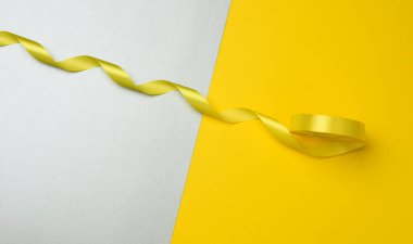 Sarı-gri arka planda süsleme için bükülmüş sarı tekstil kurdelesi, yukarıdan görünüm