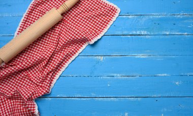 Yuvarlak iğne ve katlanmış kırmızı-beyaz pamuklu mutfak peçetesi ahşap mavi arka planda, üst manzara, kopyalama alanı