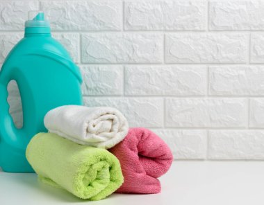 Beyaz bir rafta plastik bir şişe sıvı çamaşır tozu ve katlanmış havlular.