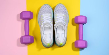 Bir çift beyaz kadın spor ayakkabısı ve renkli bir arka planda mor halterler.