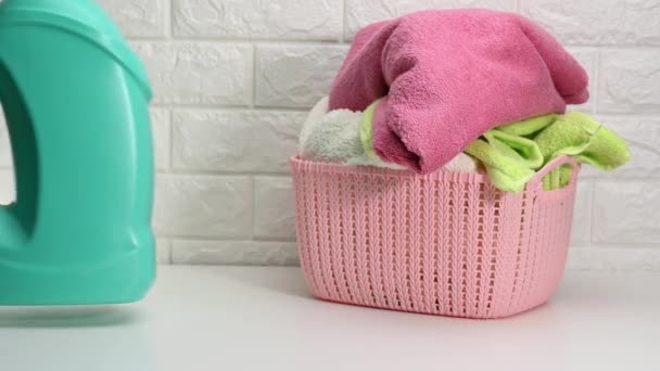 一个塑料篮子 上面有洗过的干毛巾和一个装有液体洗涤剂的橙色瓶子 放在一面白色的砖墙的后面 — 图库视频影像