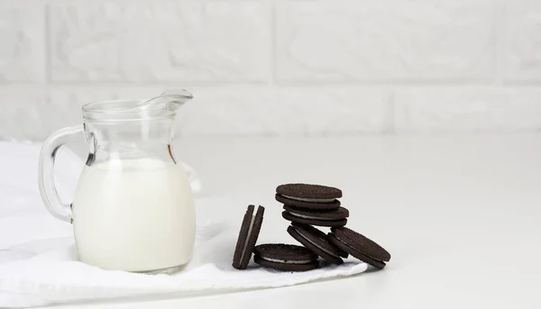 full glass carafe of milk and a stack of chocolate chip cookies on a white table