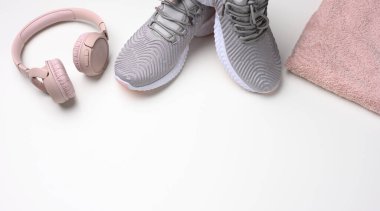 Bir çift gri tekstil spor ayakkabısı, kablosuz kulaklık ve beyaz arka planda tekstil pembe havlu. Spor için hazır, koşuyor