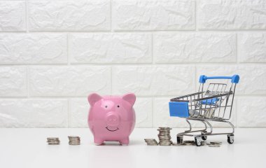 Pembe seramik domuz kumbarası ve beyaz arka planda bir yığın bozuk para. Tasarruf konsepti, bütçe planlaması. Gelir artışı