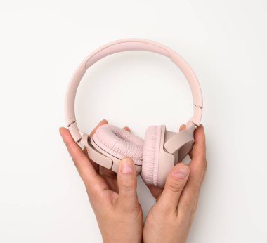 Beyaz arka planda pembe kablosuz kulaklık tutan iki kadın el var.