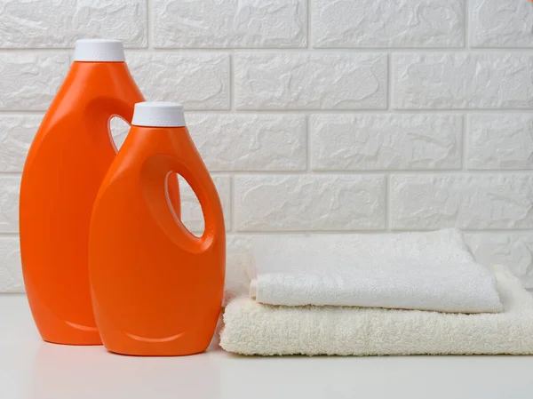 Dwie Pomarańczowe Plastikowe Butelki Płynnego Detergentu Stos Ręczników Białej Półce — Zdjęcie stockowe