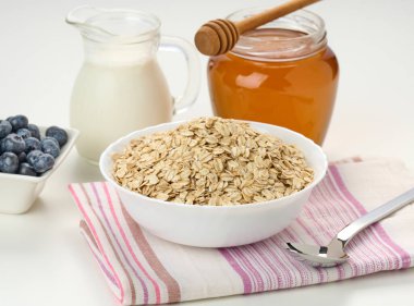 Sabah kahvaltısı, seramik tabakta çiğ yulaf ezmesi sütü bir sürahide ve bal kavanozda beyaz bir masada, kapat.