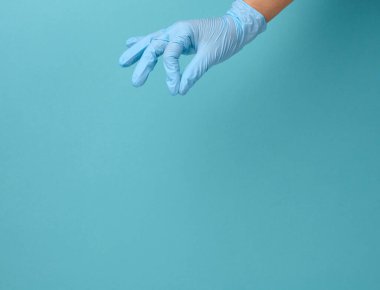Mavi tıbbi eldivenli doktorun elinde mavi arka planda bir nesne var. Uzayı kopyala, herhangi bir nesneyi tut