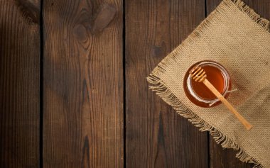 Şeffaf cam bir kavanozda taze bal ve kahverengi bir masada ahşap bir kaşık, üst manzara, boşluğu kopyala
