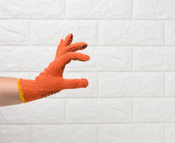 female hand in an orange work protective glove against the background of a white brick wall, the hand conditionally holds an object