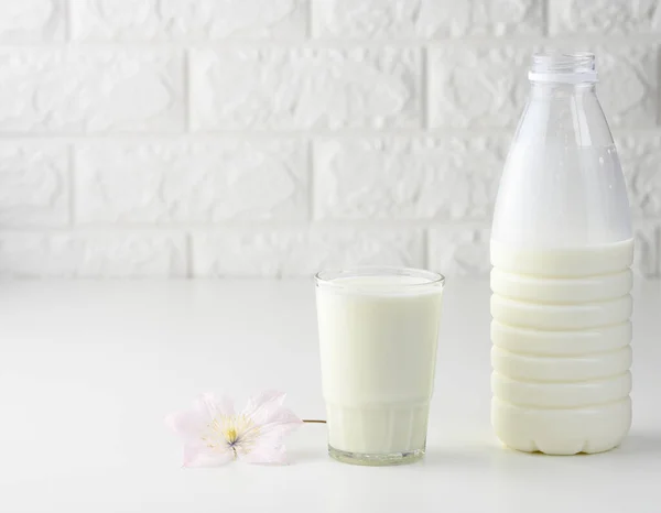 full plastic milk bottle and glass cup on white table, brick wall background