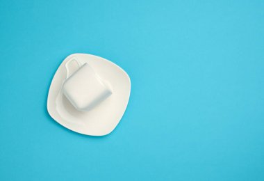 Mavi arkaplanda boş beyaz seramik bardak ve fincan tabağı, üst görünüm, boşluk kopyala