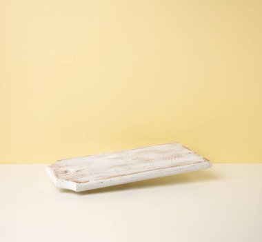 Sarı arka planda boş beyaz ahşap mutfak tahtası, çatal bıçaklar.