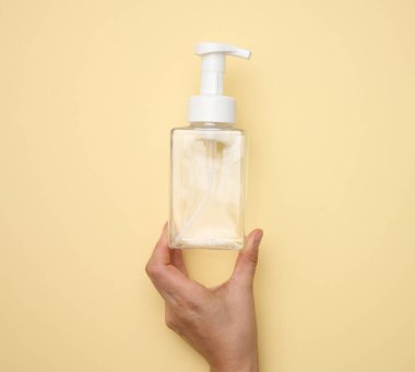 Kadın eli, sıvı ürünler, sabun veya bej arka planda şampuan için kullanılan boş plastik bir kap tutuyor.