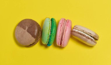 Colorful macarons are laid out in a row on a bright yellow background. Top view.