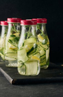 İçi salatalık, limon dilimleri ve nane yapraklarıyla dolu kırmızı kapaklı büyük şişeler.