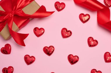 El işi kağıdına sarılı bir hediye kutusu ve pembe arka planda kırmızı saten bir fiyonkla bağlanmış.