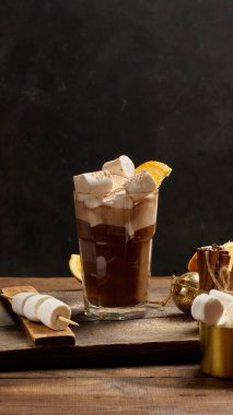 Bir bardak sıcak çikolata, üzerinde beyaz lokum parçaları olan tahta bir masa.