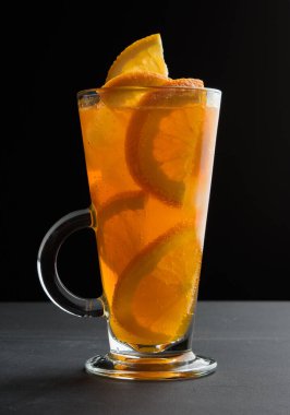 Siyah bir masada, portakal dilimli, uzun bir bardakta, ferahlatıcı bir limonata.