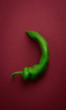 Zengin bir bordo arka planda uzun, kıvrımlı yeşil kırmızı biber. Sıcaklık, baharat ve yiyecek kavramı.