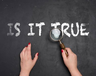 Bir kadının elleri beyaz tebeşirle yazılmış mesajın üzerinde klasik bir büyüteç tutuyor. Siyah bir karatahtanın üzerinde doğruluk ve gerçeği araştırmayı sembolize ediyor..