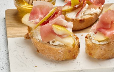 İtalyan bruschetta 'sına yakın bir dilim jambon, armut, yumuşak peynir ve susamlı ekmek. Tabak hafif mermer bir tahtanın üzerinde servis edilir.