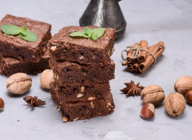 Nane yaprağı, tarçın çubuğu, yıldız anason ve ceviz ile süslenmiş, cevizli, cevizli ve cevizli üç kare çikolatalı kek yığını..