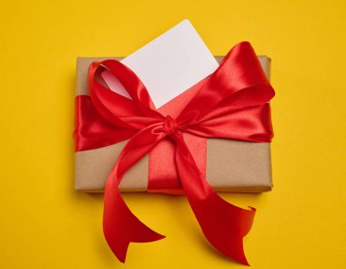 El işi kağıdına sarılı bir hediye kutusu ve sarı arka planda büyük kırmızı saten bir fiyonk ile bağlanmış.
