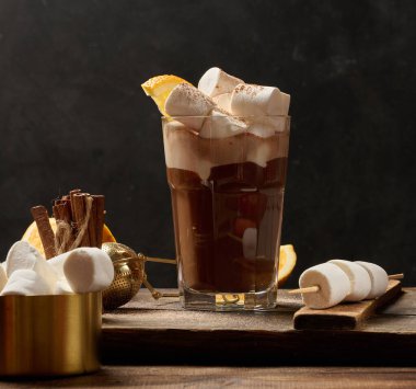 Bir bardak sıcak çikolata, üzerinde beyaz lokum parçaları olan tahta bir masa.