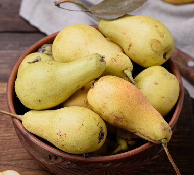 Tahta bir masada kahverengi bir kasede olgun sarı armutlar.