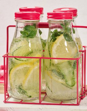 İçi salatalık, limon dilimleri ve nane yapraklarıyla dolu kırmızı kapaklı cam şişeler.