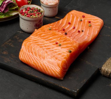 Siyah bir tahta üzerinde taze somon balığının yakın plan çekimi. Balığın zengin turuncu rengi ve kıtır kıtır bir dokusu vardır..