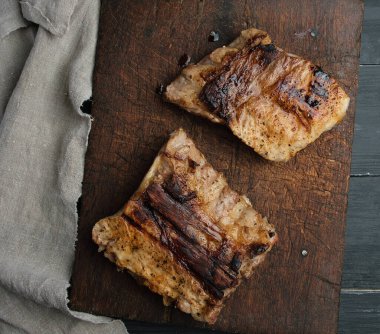 Eski ahşap bir tahtanın üstünde iki parça kızarmış et.