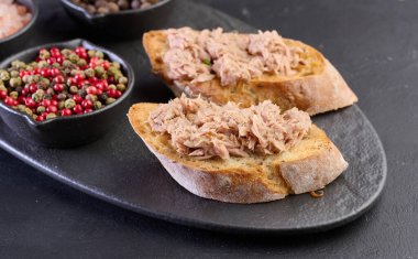 Siyah tahtada ton balıklı bruschetta ve yanında baharatlar..