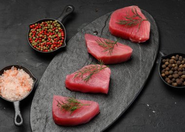 Kara tahtada çiğ ton balığı parçaları, yakınlarda baharatlar. Üst görünüm