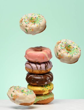 Çeşitli dolguları ve jöleleri olan bir yığın donut, birkaç tane de yukarı doğru yükselen. Yeşil arkaplan.