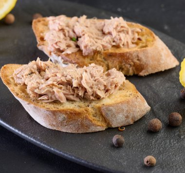 Kızarmış ekmek, doğranmış pembe ton balığı ve limon dilimleri.